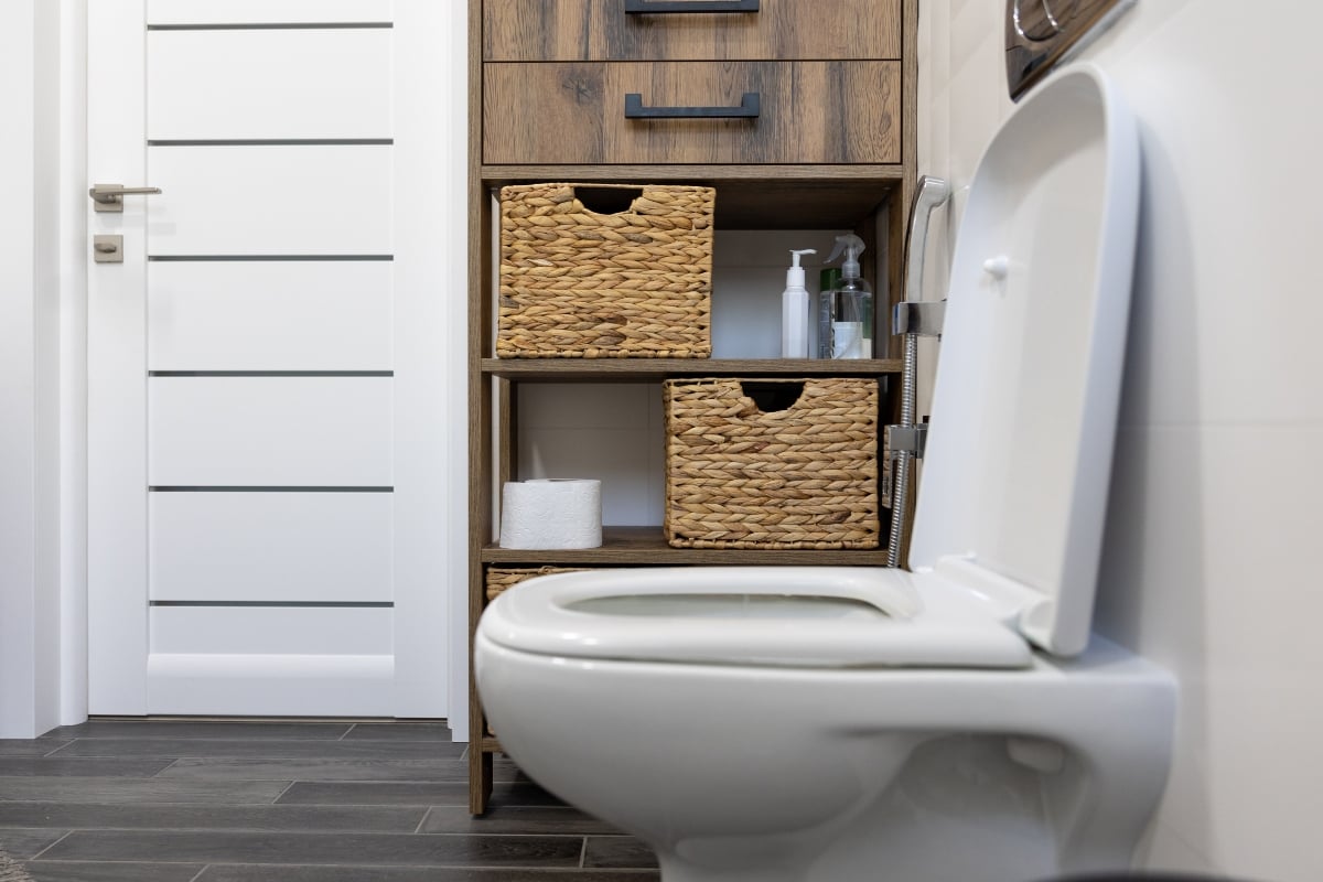 Fixing a running toilet in a modern bathroom with wooden shelves.