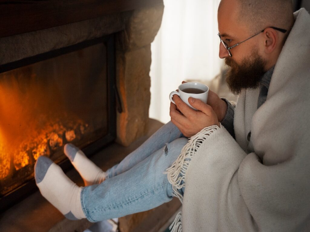A man wrapped in a blanket sitting next to a fireplace.