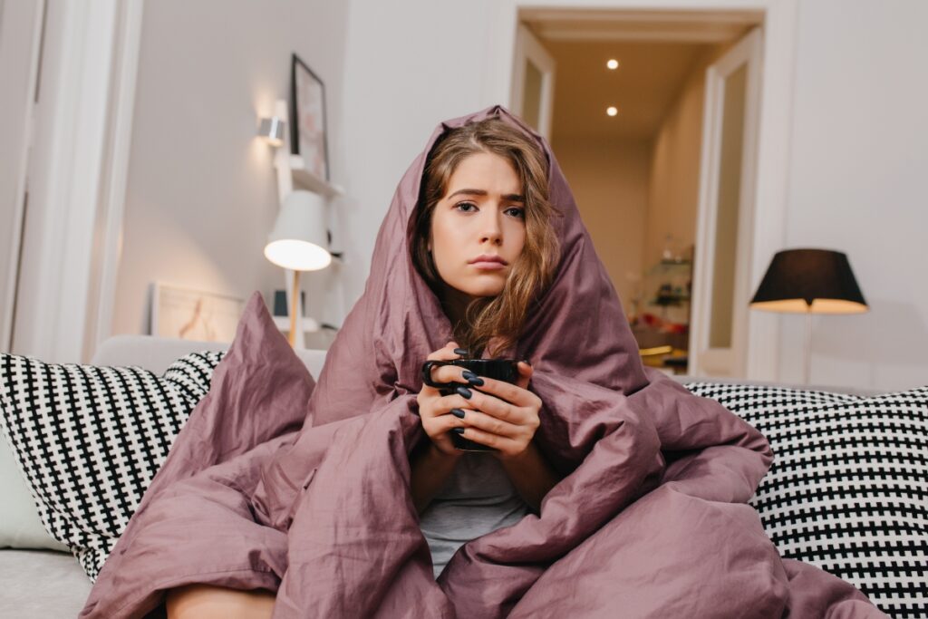 A woman with a blanket and a mug, freezing because her heating isn’t working.