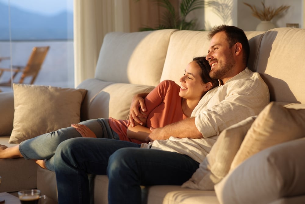 Happy,Couple,Enjoying,Sunset,Together,Sitting,On,A,Sofa,At